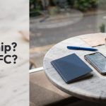 A plain dark-blue booklet and a smartphone on a marble cafe table next to a cappuccino.
